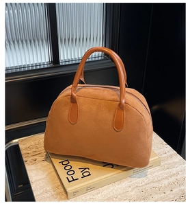 Close-up of brown suede Boston bag with leather handles on marble and book background