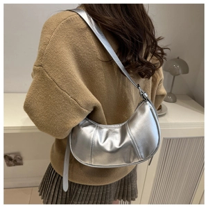 Silver crescent underarm bag with metallic mirror finish worn by a model in a cozy room