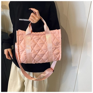 Pink quilted nylon handbag with diamond pattern held by model against a white wall