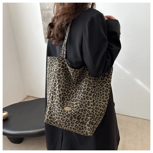 Détail d'un grand sac cabas à imprimé léopard avec logo, porté avec un manteau noir
