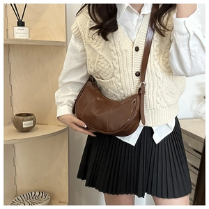 Brown semi-circle leather bag worn with cream vest in a warm domestic interior