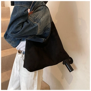 Detail of minimalist black matte suede hobo bag worn by a model with wide strap and large capacity