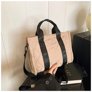 Detail of beige quilted handbag with black fabric handles and detachable crossbody strap