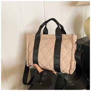 Detail view of beige quilted rhombic pattern handbag with black nylon straps