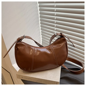 Detail of a brown half-moon underarm bag with vintage oil-wax texture and stitching