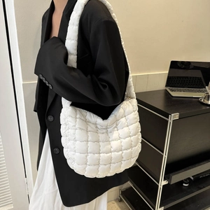 Lifestyle shot of white quilted puffy shoulder bag styled on model in minimalist office