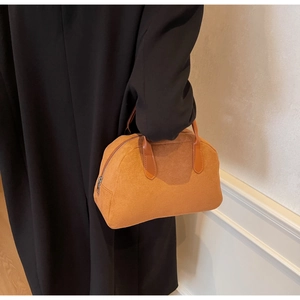 Detailed texture of caramel suede Boston bag held by model wearing a black winter coat