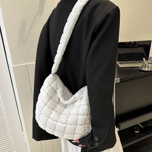 Close-up of a white quilted cloud bag with wide shoulder strap on a black blazer