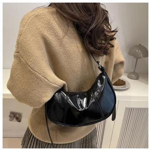 Détail d'un sac à bandoulière noir brillant en forme de demi-lune avec coutures épurées