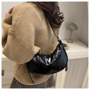 Detail of black glossy half-moon bag on shoulder with silver hardware and chic stitching