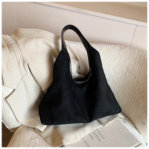 Detail of black suede tote bag with vertical stitching on a beige suit backdrop