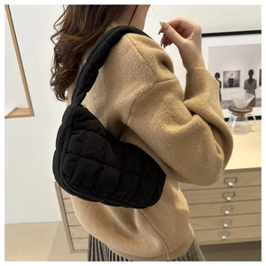 Side view of puffy black quilted cloud bag worn with a beige sweater in a warm home setting