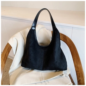 Detail of minimalist black suede hobo bag on beige blazer with soft side lighting