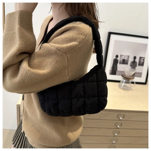 Close-up of black quilted shoulder bag featuring soft puff texture on a female model