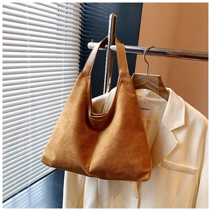 Detail of a brown suede tote bag with wide leather strap on a classic beige blazer