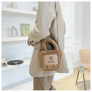 Détail du sac seau en peluche marron avec écusson en cuir et bandoulière réglable