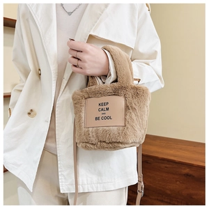 Détail du sac seau en peluche avec écusson en cuir et longue bandoulière marron