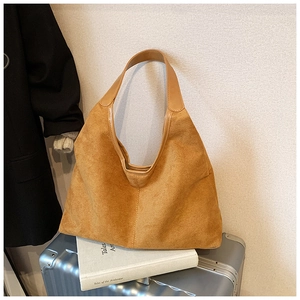Detail of a brown suede tote bag resting on a silver suitcase for a commute concept