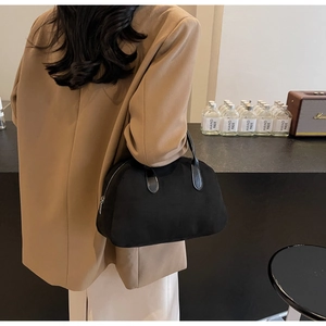 Detail of black suede Boston bag with leather handles held by a model in a beige suit