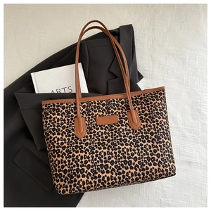 Detailed view of leopard print tote bag with brown leather handles on soft fabric