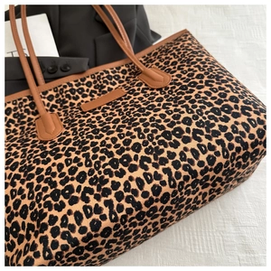 Detail of leopard print tote bag with brown leather straps on stylish white fabric background
