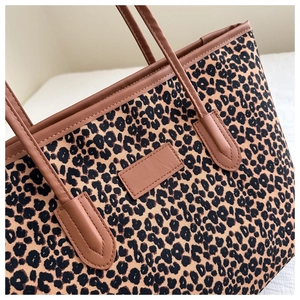 Detail of leopard print fabric tote bag with brown leather handles and stitching