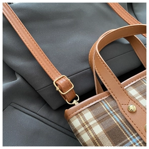 Detail of golden adjustable buckle and metal rivets on brown plaid fabric tote bag