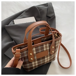 Detailed view of plaid tote bag with brown leather handles and golden rivet accents