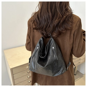 Detail of dark grey vintage leather backpack with vertical silver zippers on dark blazer