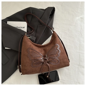 Detail of suede shoulder bag featuring a dark brown leather butterfly patch with lace-up ties
