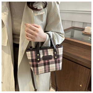 Detail of pink plaid tote bag with brown leather handles and golden rivets