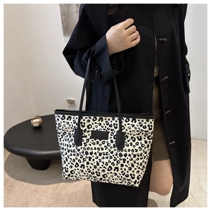 Detail of a large leopard print tote bag with black leather handles shown in a home setting