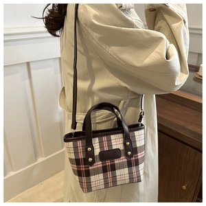 Detail of plaid bucket bag with gold rivets styled on a beige trench coat
