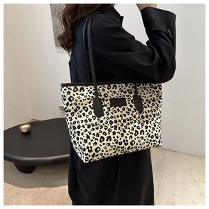 Detailed view of leopard print tote bag on shoulder with black logo patch and canvas texture