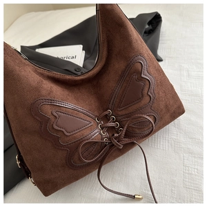 Detail of brown suede shoulder bag with butterfly leather patch and lace-up design