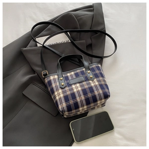 Flat lay of blue plaid tote bag with black handles and gold rivets on a beige surface
