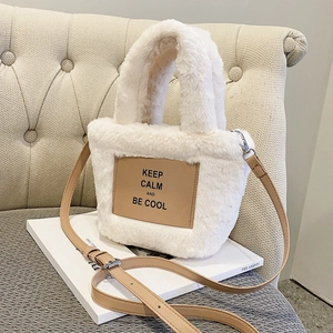 White plush tote bag with leather tag and adjustable strap on a leather sofa
