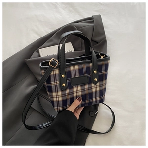 Detailed shot of plaid fabric tote with black leather trim and gold rivet accents