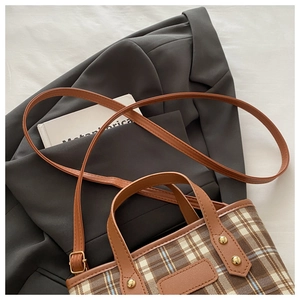 Close-up of checkered tote bag with brown leather straps and gold metal rivet details