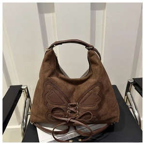 Detail of brown suede hobo bag featuring decorative butterfly appliqué and tie strings