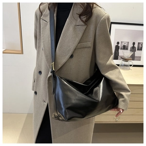 Sac bandoulière minimaliste en cuir noir mat porté par un mannequin dans un studio