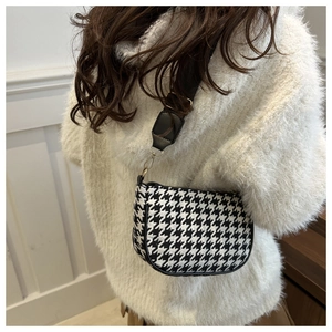 Detail of black and white houndstooth saddle bag with golden metal hardware and strap