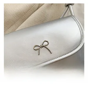 Detail of silver faux leather shoulder bag featuring a metallic bow hardware decoration