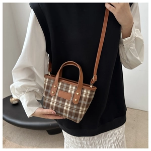Detail of brown plaid tote bag with leather handles and gold rivets on a model