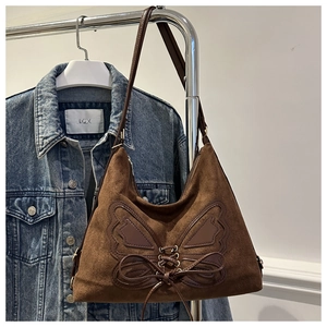Detailed view of brown suede shoulder bag featuring a large butterfly patchwork and bow tie