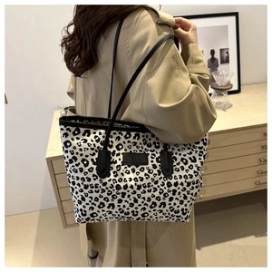 Detail of stylish leopard print tote bag with black leather handles on beige coat