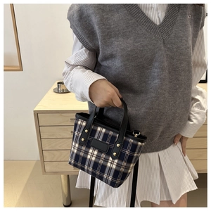 Detail of navy blue plaid handbag with black leather handle and gold rivet accents