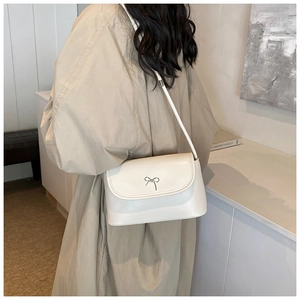 Detail of cream white crossbody bucket bag featuring a small silver metal bow decoration