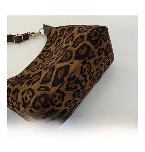 Close-up of fluffy leopard print fabric texture and adjustable brown strap on a bag