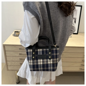 Close-up of a plaid canvas tote bag with black leather handles and gold rivet details